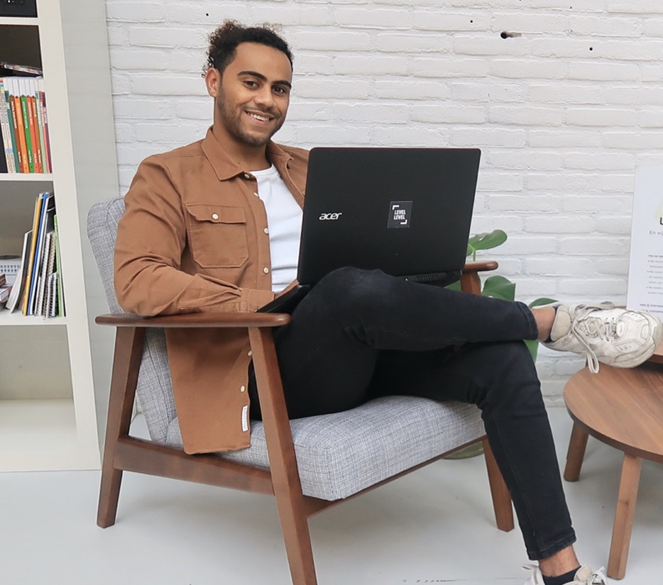 Noah, sitting behind his laptop, smiling at the camera.